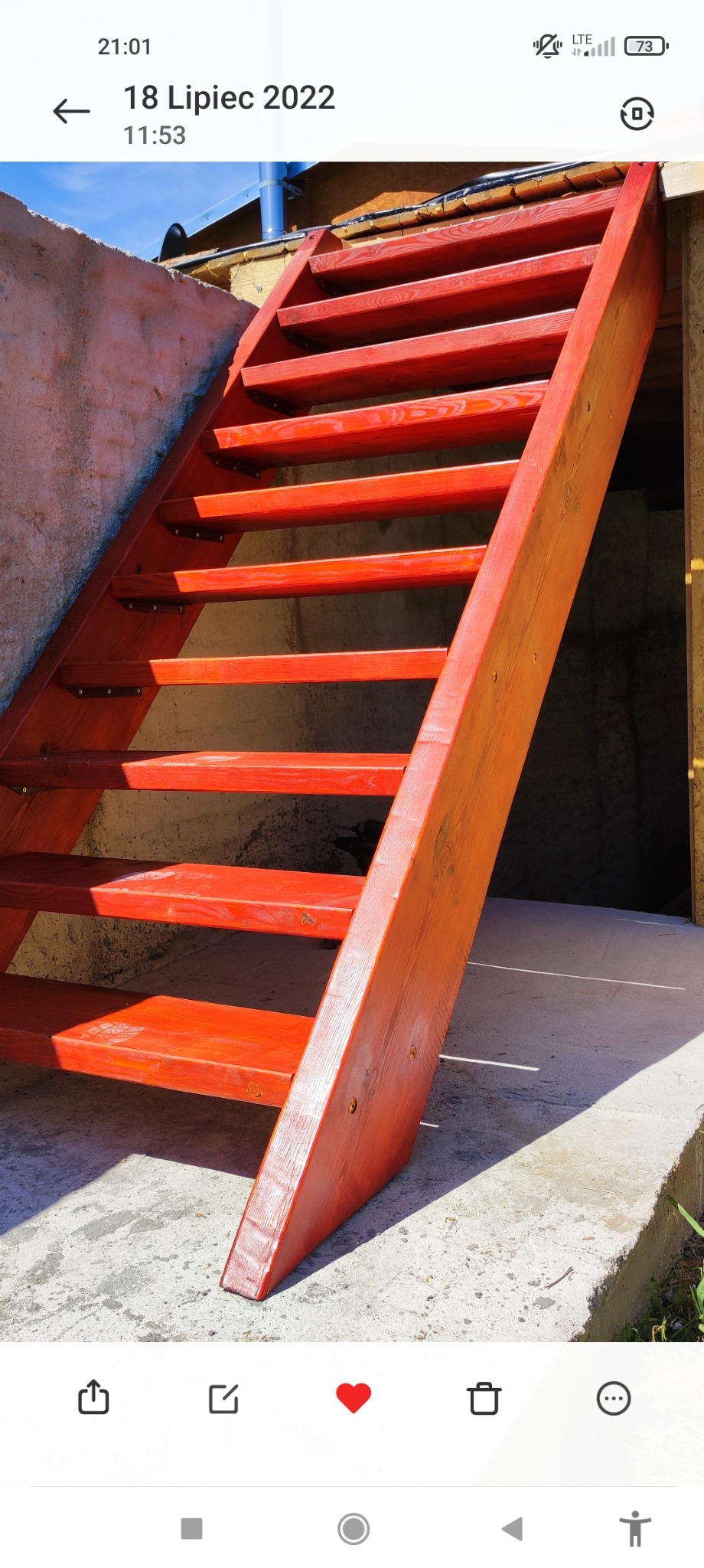 Czerwone drewniane schody zewnętrzne prowadzące do piwnicy, z widoczną fakturą drewna i betonową posadzką.