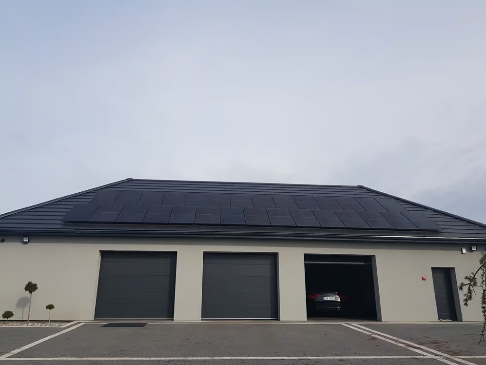 Dom z szarymi panelami fotowoltaicznymi na dachu i trzema garażami, w jednym z nich zaparkowany samochód.