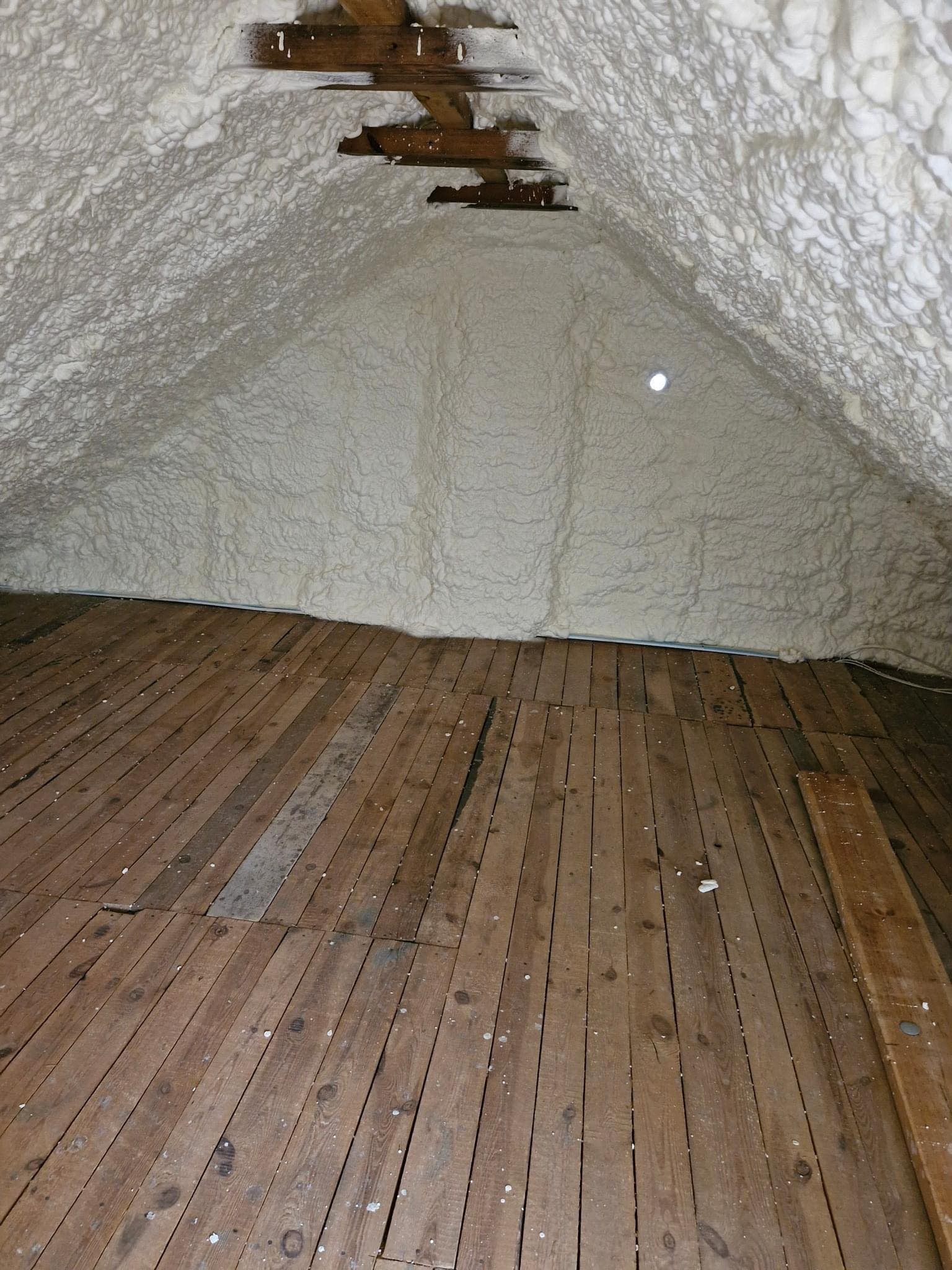 Poddasze po ociepleniu pianką poliuretanową, widoczne drewniane belki i stara drewniana podłoga.