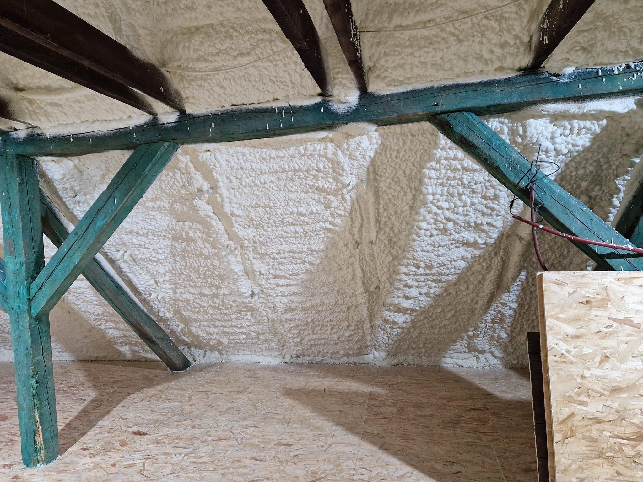 Poddasze ocieplone pianką poliuretanową, widoczne drewniane elementy konstrukcyjne pomalowane na zielono, podłoga wyłożona płytami OSB.