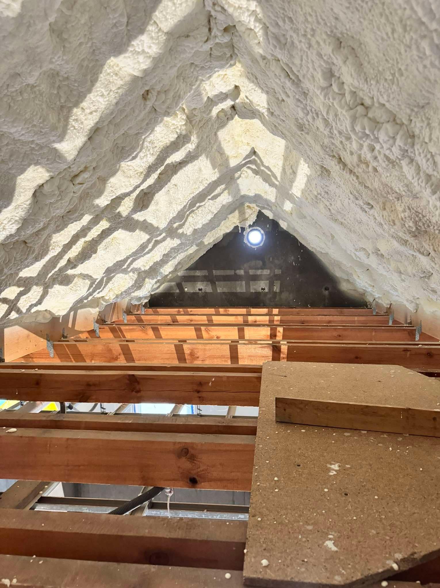 Poddasze ocieplone pianą PUR z widoczną konstrukcją drewnianą, oświetlone lampą sufitową i wpadającym światłem słonecznym.