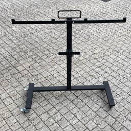 Sebastian Drewniak - Czarny, metalowy stojak na kółkach, prawdopodobnie do ekspozycji odzieży lub innych przedmiotów, na szarym brukowanym podłożu.