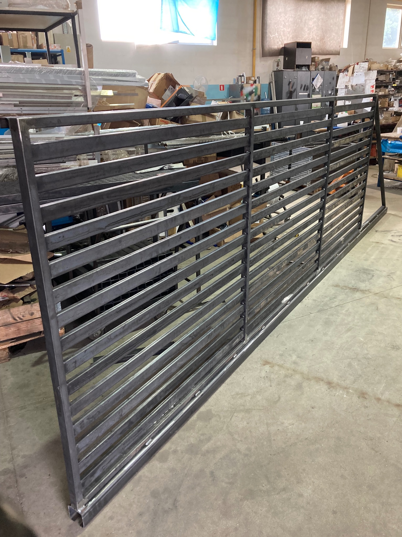 Surowa, metalowa konstrukcja bramy wjazdowej z poziomymi szczeblami, widoczna w hali produkcyjnej przed malowaniem lub montażem.