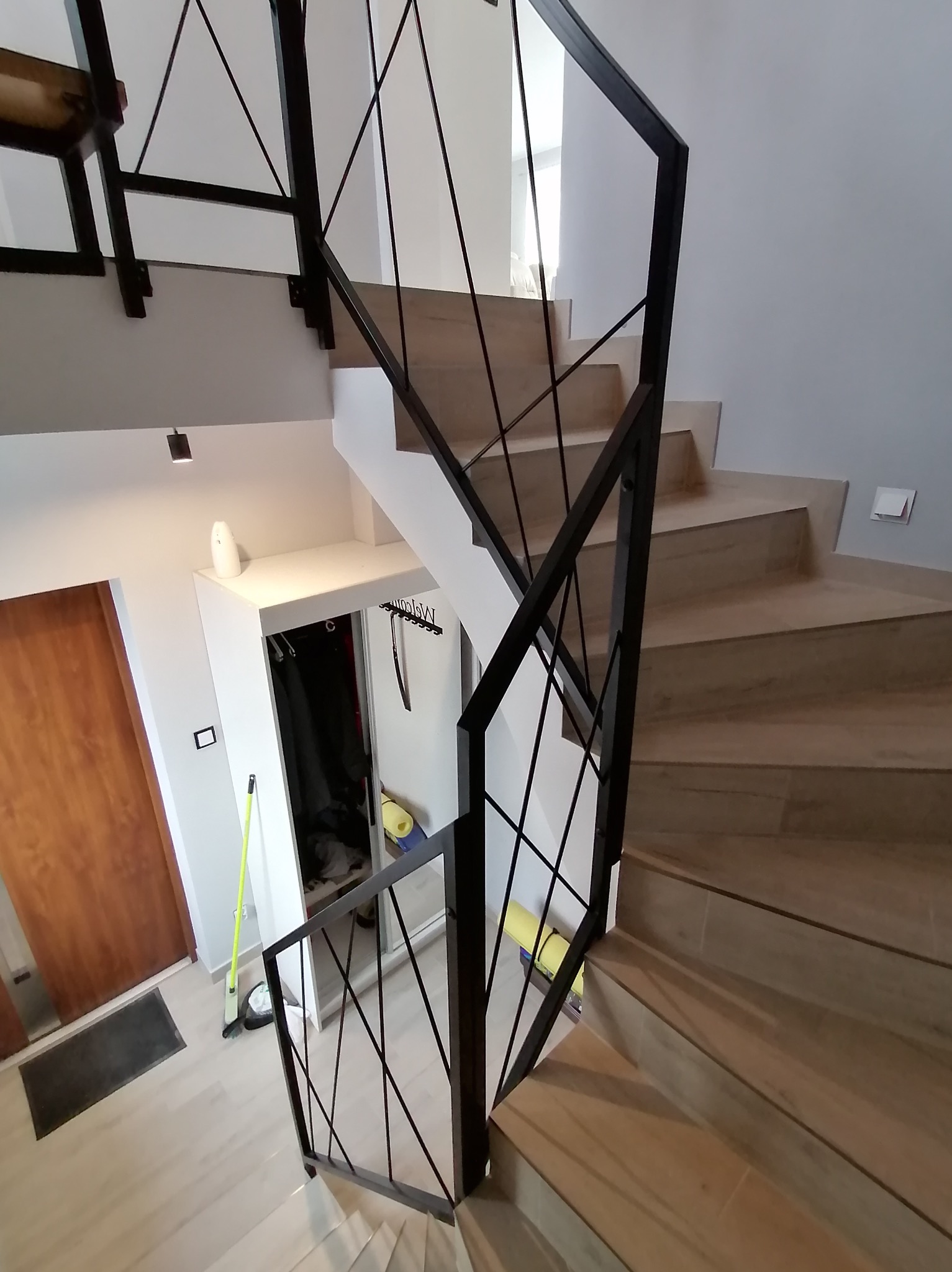 Nowoczesna balustrada schodowa z czarnych, metalowych prętów na jasnych, drewnopodobnych schodach w jasnym wnętrzu domu.