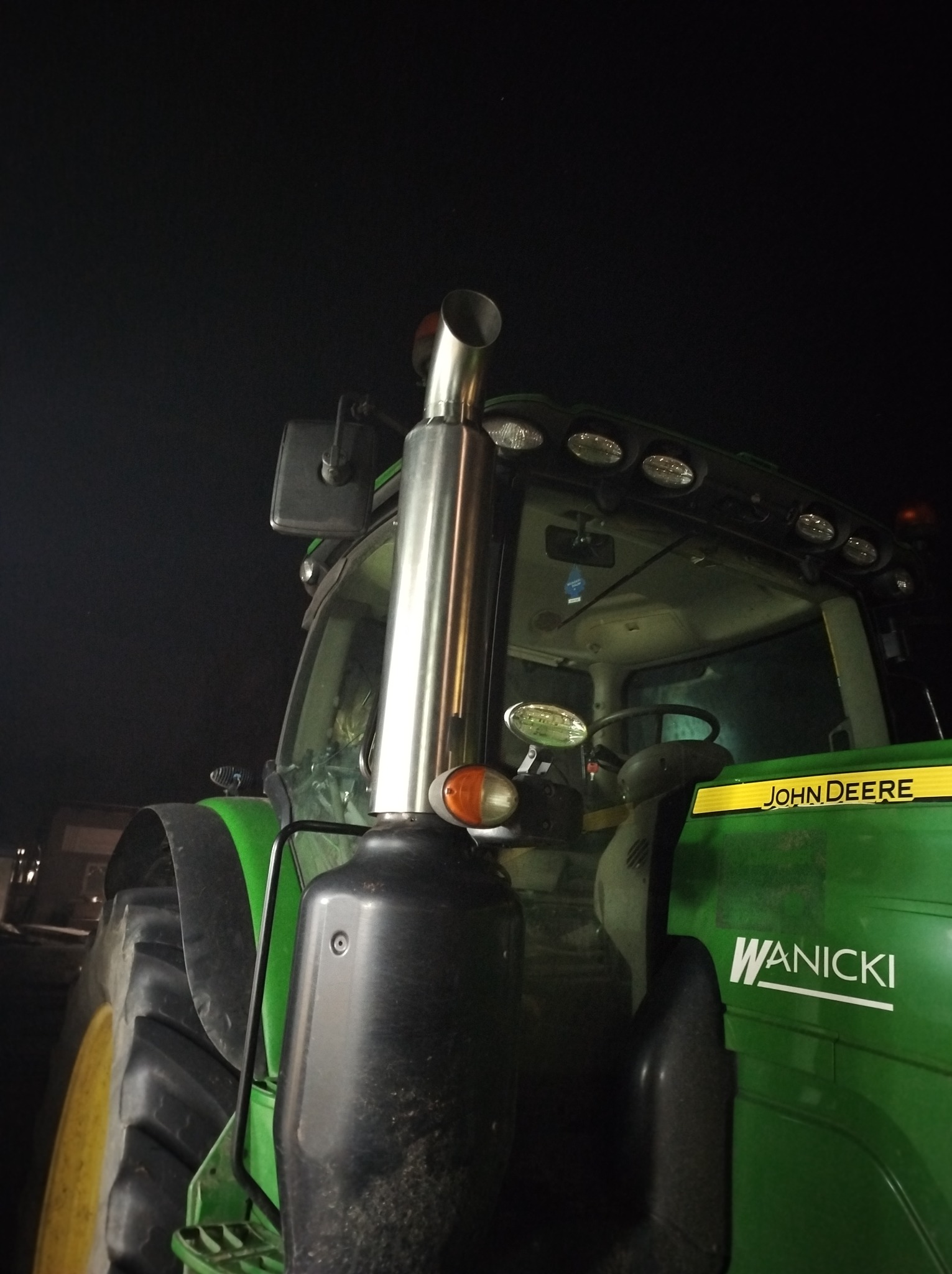 Zielony traktor John Deere z chromowanym kominem i napisem 'WANICKI' na tle nocnego nieba.