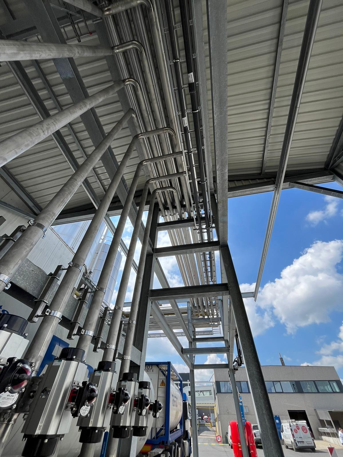 Skomplikowany system rur ze stali nierdzewnej, zamontowany pod zadaszeniem, widoczny z dołu pod kątem. Elementy konstrukcyjne i niebieskie niebo w tle.