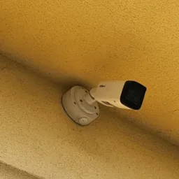 Kamera przemysłowa Dahua zamontowana na żółtej, teksturowanej ścianie wewnątrz budynku, widok z dołu.