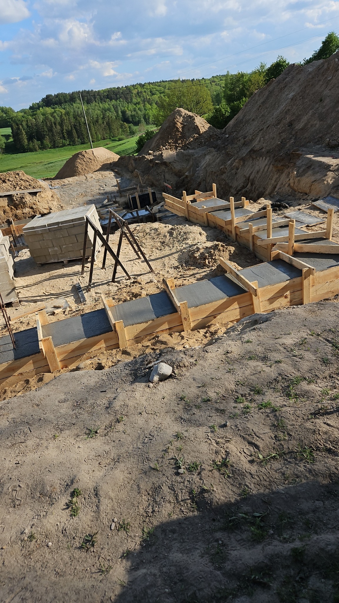 Przygotowanie fundamentów: drewniane szalunki wypełnione świeżym betonem, w tle ziemia i zieleń drzew.