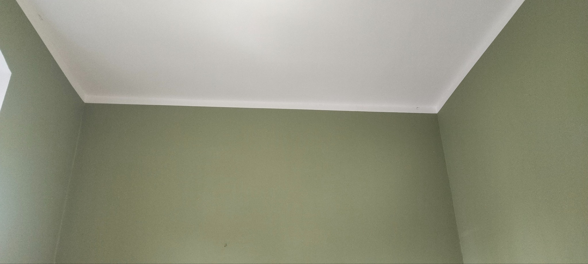 Pomieszczenie po odświeżeniu: biały sufit z delikatnym sztukateryjnym wykończeniem styku ze ścianą w odcieniach oliwkowej zieleni.