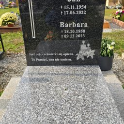 Mariusz Pietraszko Grawerowanie I Liternictwo Taxi - Czarny, polerowany pomnik z wygrawerowanym krzyżem i inskrypcjami, otoczony cmentarnym krajobrazem z kwiatami w donicach.