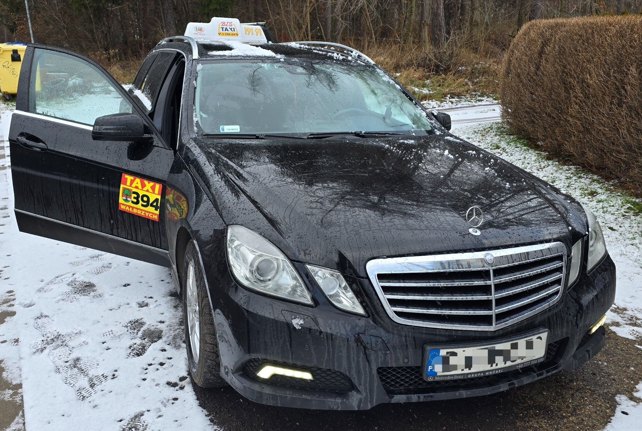 Czarna taksówka Mercedes z otwartymi drzwiami stojąca na śniegu.