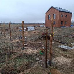 Wood Escape Homes - Budowa domu szkieletowego: widok na drewniany budynek w trakcie wznoszenia, z widocznymi słupami fundamentowymi i elementami konstrukcyjnymi w surowym krajobrazie.