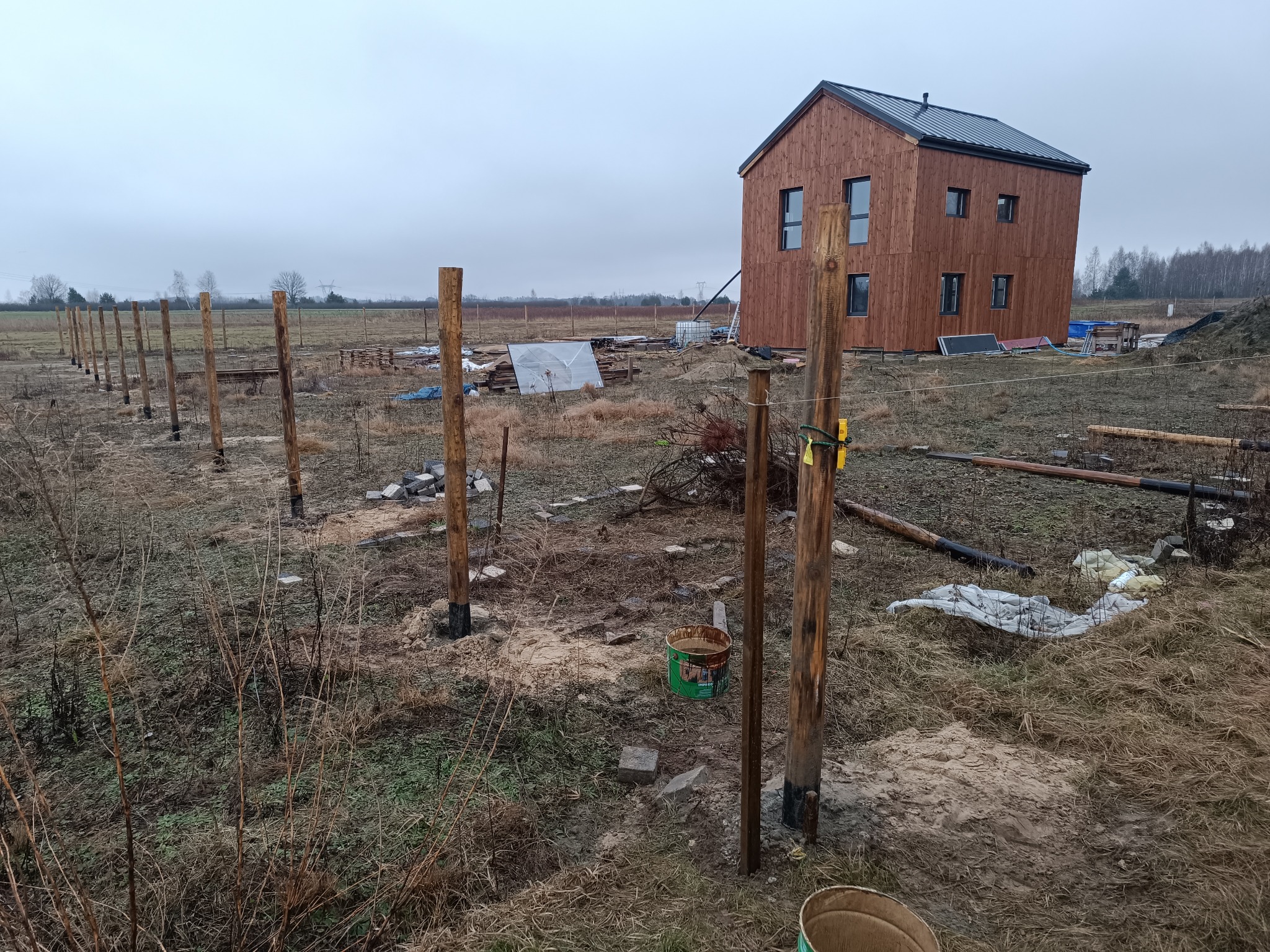 Budowa domu szkieletowego: widok na drewniany budynek w trakcie wznoszenia, z widocznymi słupami fundamentowymi i elementami konstrukcyjnymi w surowym krajobrazie.