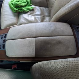 Wypolerowani Ernest Milewski - Czyszczenie skórzanego podłokietnika samochodowego, widoczna różnica między wyczyszczoną lewą stroną a brudną prawą stroną, na siedzeniu leży zielona ściereczka z mikrofibry.