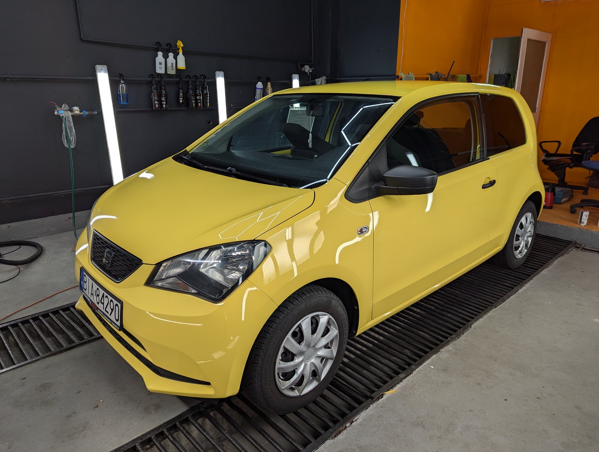 Żółty samochód Seat Mii po przyciemnianiu szyb, widoczne ciemne szyby, czarne felgi i reflektor. Samochód stoi na metalowej kracie w warsztacie.