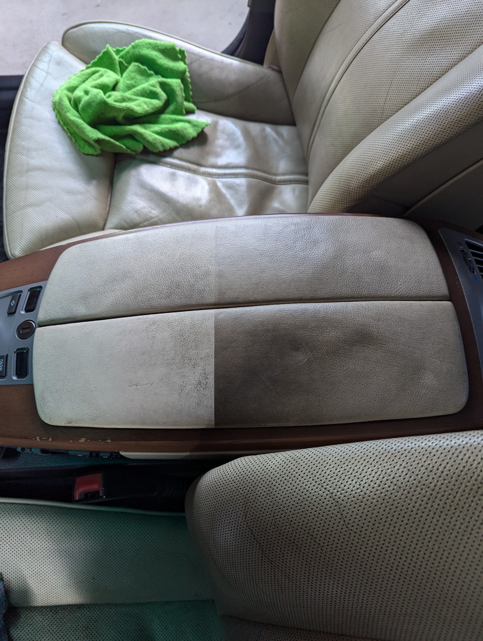 Czyszczenie skórzanego podłokietnika samochodowego, widoczna różnica między wyczyszczoną lewą stroną a brudną prawą stroną, na siedzeniu leży zielona ściereczka z mikrofibry.