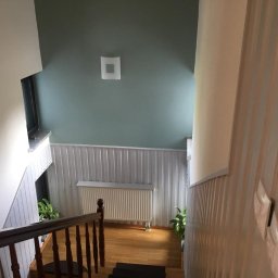 PROJEKT Pro. - Klatka schodowa po malowaniu ścian na kolor zielony i biały, z drewnianymi schodami i grzejnikiem pod oknem, widok z góry.