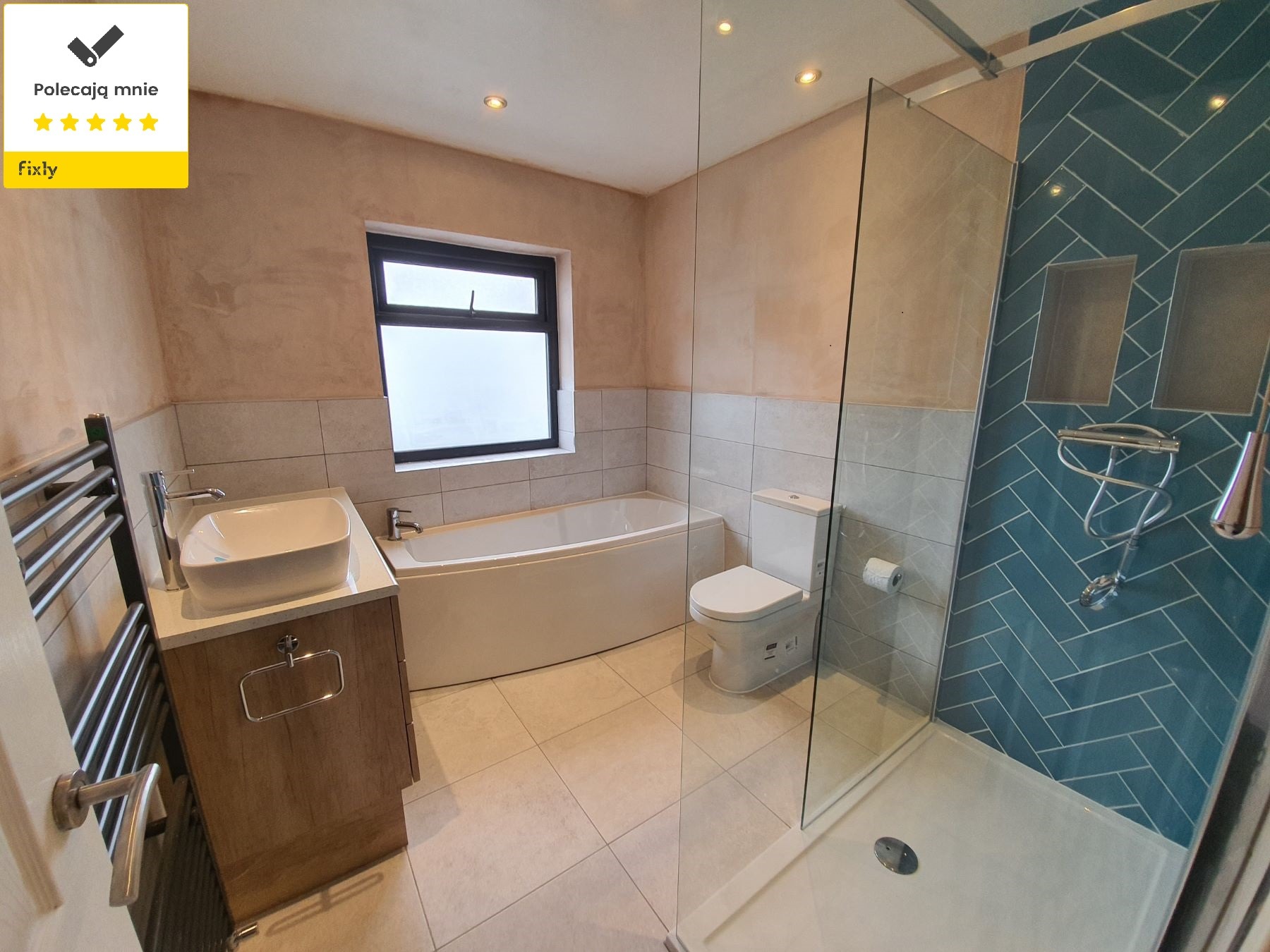 Nowoczesna łazienka po remoncie z kabiną prysznicową oddzieloną szklaną ścianką, umywalką na szafce z drewnianym frontem, grzejnikiem drabinkowym i wykończoną ścianą z niebieskich płytek ułożonych...