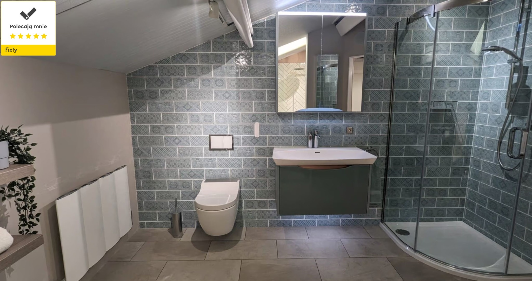 Nowoczesna łazienka na poddaszu z kabiną prysznicową, umywalką z szafką w kolorze butelkowej zieleni i toaletą w zabudowie, wykończona płytkami w odcieniach szarości z dekoracyjnym wzorem.
