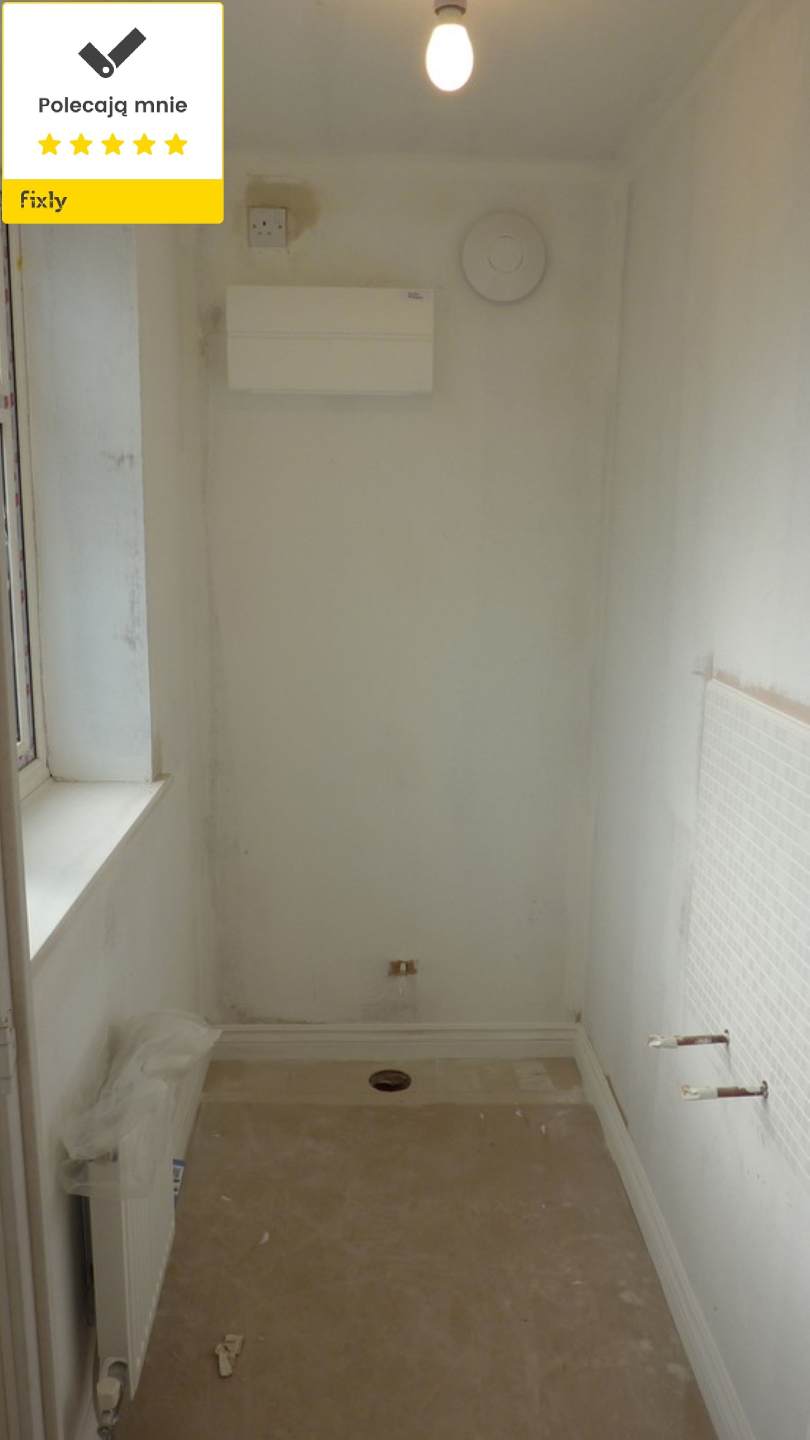 Łazienka w trakcie prac remontowych: widoczne przygotowane ściany, częściowo położona mozaika, zakryty grzejnik i otwór w podłodze. Na ścianie widoczna skrzynka elektryczna.