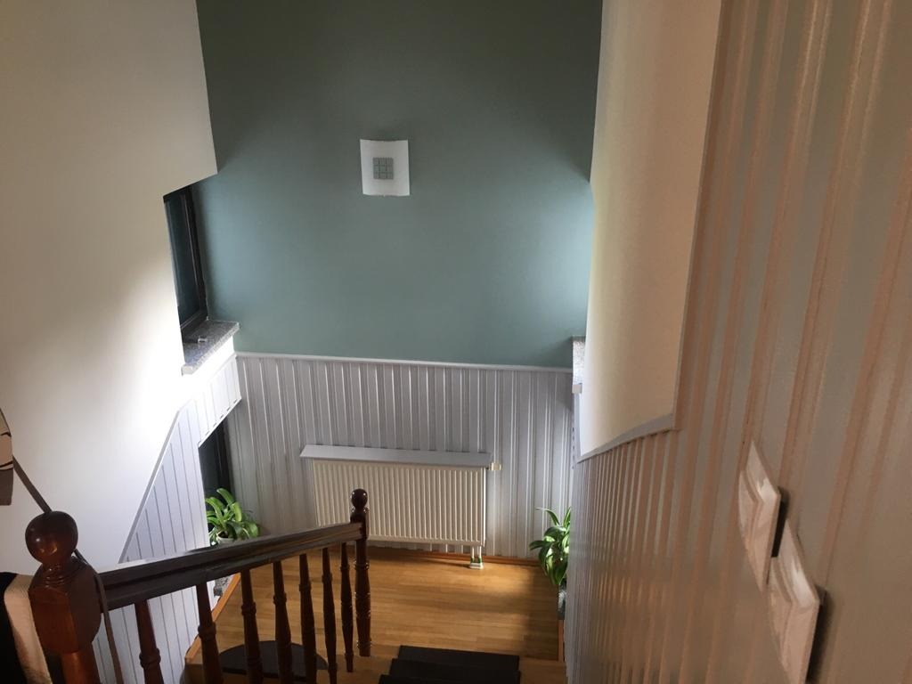 Klatka schodowa po malowaniu ścian na kolor zielony i biały, z drewnianymi schodami i grzejnikiem pod oknem, widok z góry.