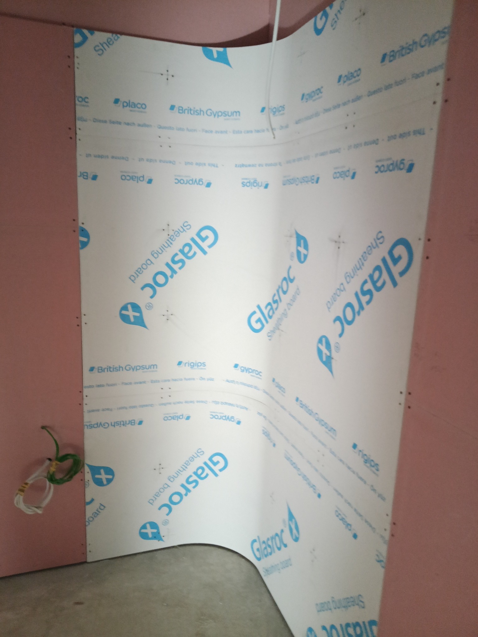 Montaż płyty Glasroc na ścianie z widocznymi śrubami i przewodami elektrycznymi. Płyta z nadrukiem logo i nazwą producenta. Widoczne łączenie płyt.