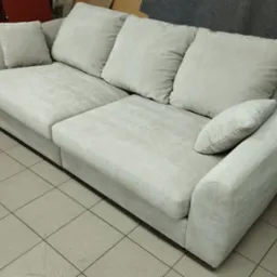 Jasnoszara, modułowa sofa z poduszkami na tle szarej ściany i podłogi z płytek ceramicznych.