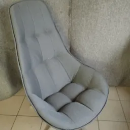 Nowoczesny fotel tapicerowany w odcieniach szarości z pikowaniem, na metalowej podstawie z trzema nogami, ustawiony na płytkach podłogowych.