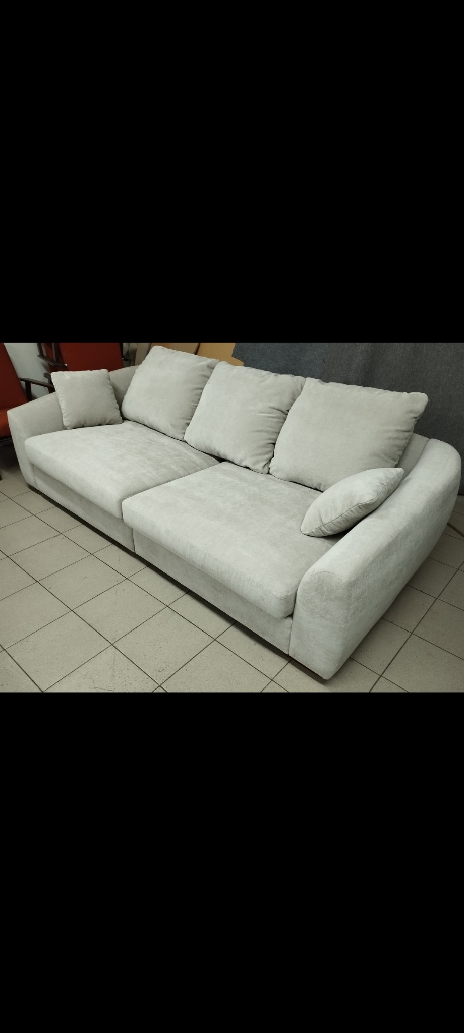 Jasnoszara, nowoczesna sofa modułowa z poduszkami na tle płytek podłogowych i fragmentu ściany.