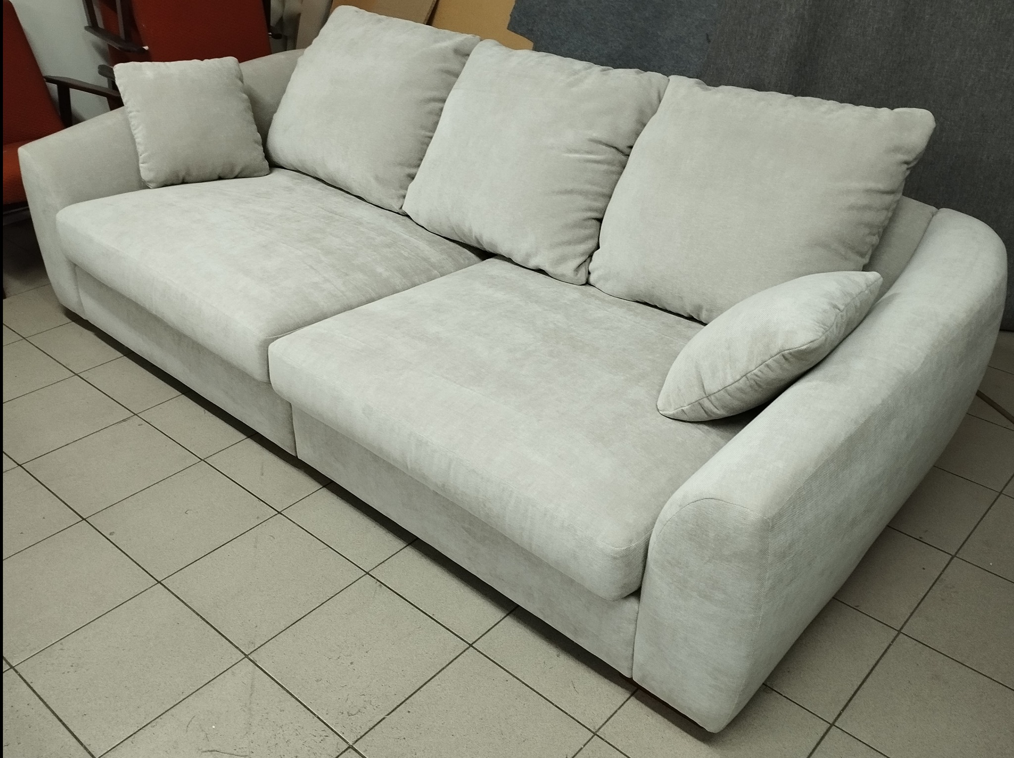 Jasnoszara, modułowa sofa z poduszkami na tle szarej ściany i podłogi z płytek ceramicznych.
