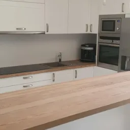 Biała kuchnia na wymiar z drewnianym blatem i wbudowanym sprzętem AGD, nowoczesny design, widok na część blatu i szafki górne.