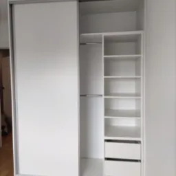 Biała szafa wnękowa z przesuwnymi drzwiami i półkami, widok z przodu. Minimalistyczny design, jasne wnętrze, drewniana podłoga. Nowoczesne rozwiązanie do przechowywania.