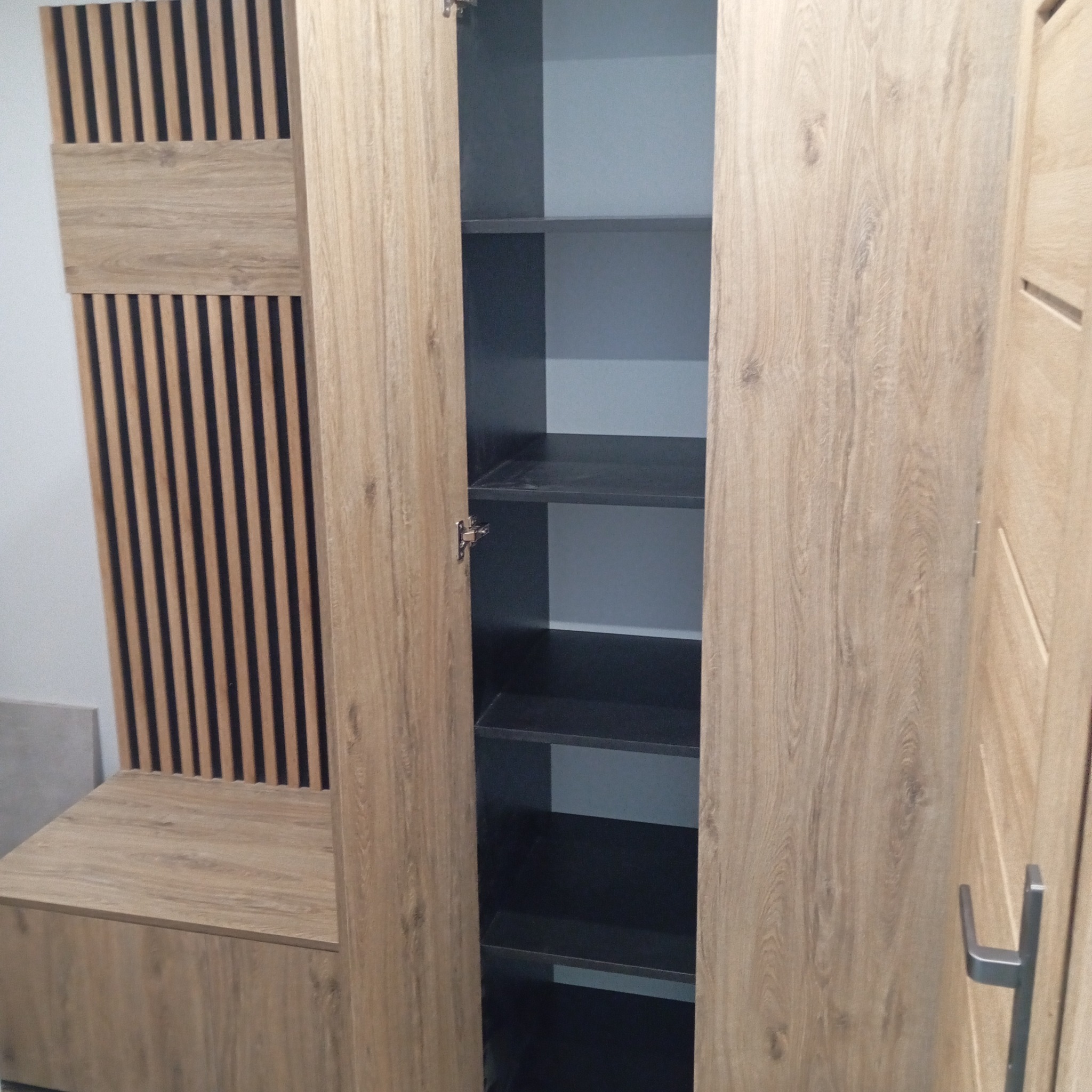 Otwarta szafa wnękowa z drewnianymi lamelami i siedziskiem, wnętrze szafy w kolorze grafitowym, półki widoczne.