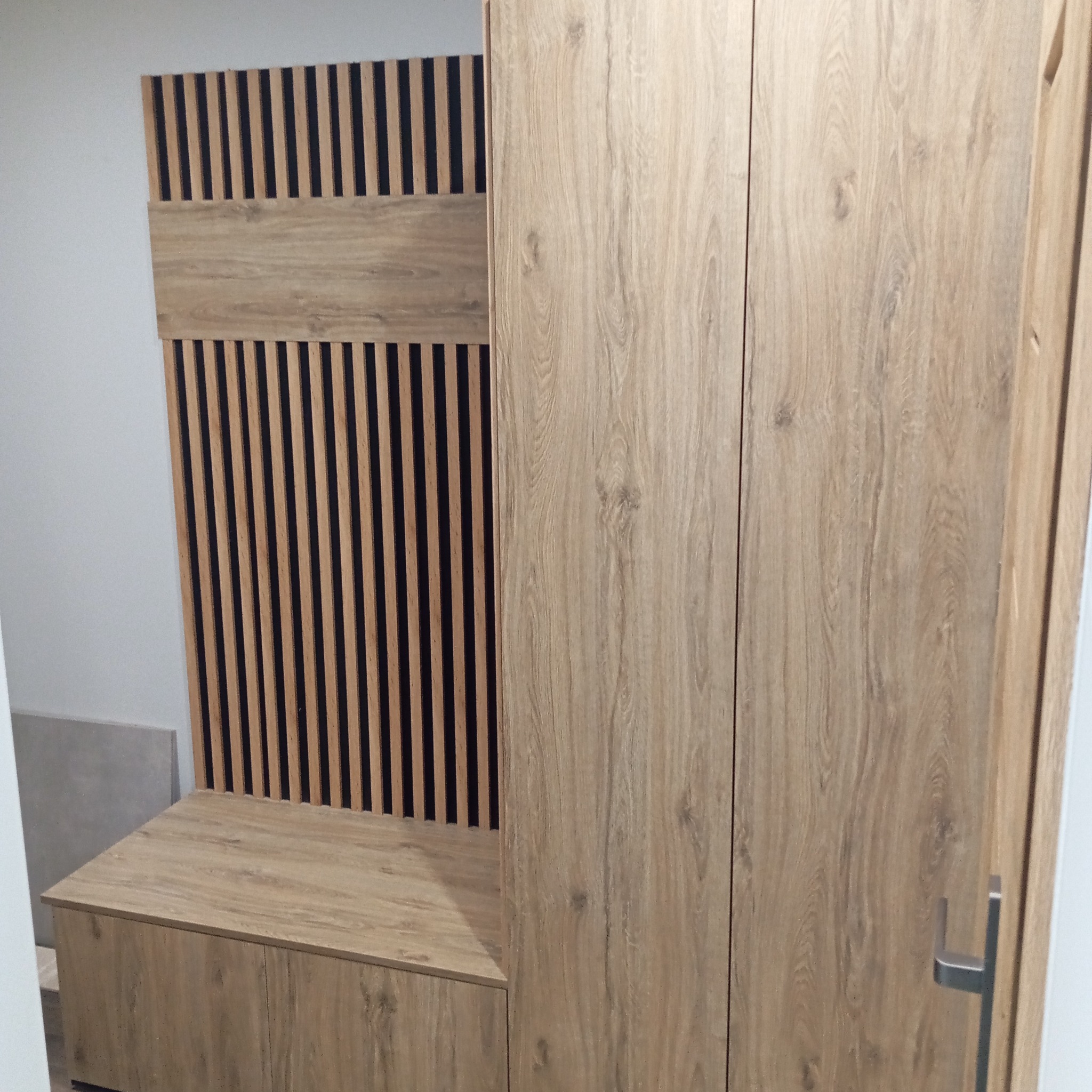 Nowoczesna szafa wnękowa z drewnianymi lamelami i frontami w odcieniach beżu. Minimalistyczny design, widoczne detale wykończenia, pionowe ułożenie lameli.