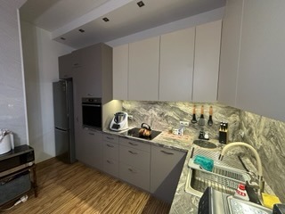 Szara zabudowa kuchenna z blatem imitującym marmur, oświetlenie LED pod szafkami, widok na zlew i sprzęty AGD. Ujęcie z perspektywy podłogi.