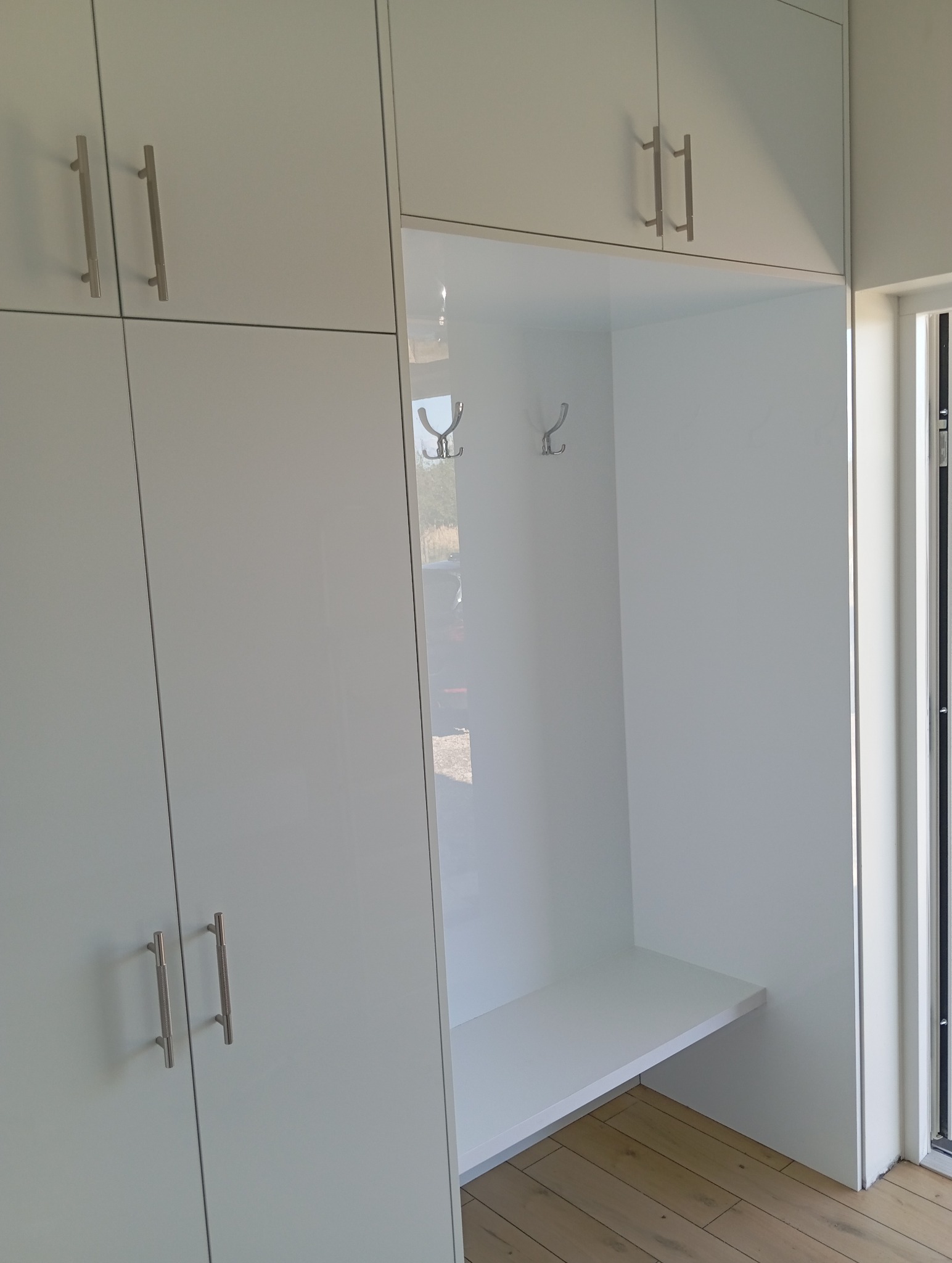 Biała szafa wnękowa z siedziskiem i wieszakami, widok z boku. Minimalistyczny design, jasne wnętrze, drewniana podłoga. Nowoczesne wykończenie.