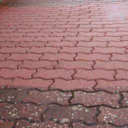 Markowe mycie - Czerwona kostka brukowa w kształcie zygzaka, częściowo umyta, z widoczną różnicą w kolorze i czystości, z rynną spustową w lewym górnym rogu.