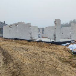 Bartłomiej Sokołowski - Budowa domu w trakcie: wzniesione ściany z betonu komórkowego na fundamencie, widoczne zbrojenia i materiały budowlane. Mglista pogoda w tle.