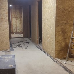 Bartłomiej Sokołowski - Wnętrze domu w trakcie budowy: surowe ściany z płyty OSB, widoczne instalacje elektryczne i oświetlenie sufitowe. Stan surowy przed wykończeniem.