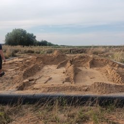 Bartłomiej Sokołowski - Przygotowanie terenu pod fundamenty domu jednorodzinnego z widocznym zarysem ścian i podkładem z piasku na działce z wysoką trawą.