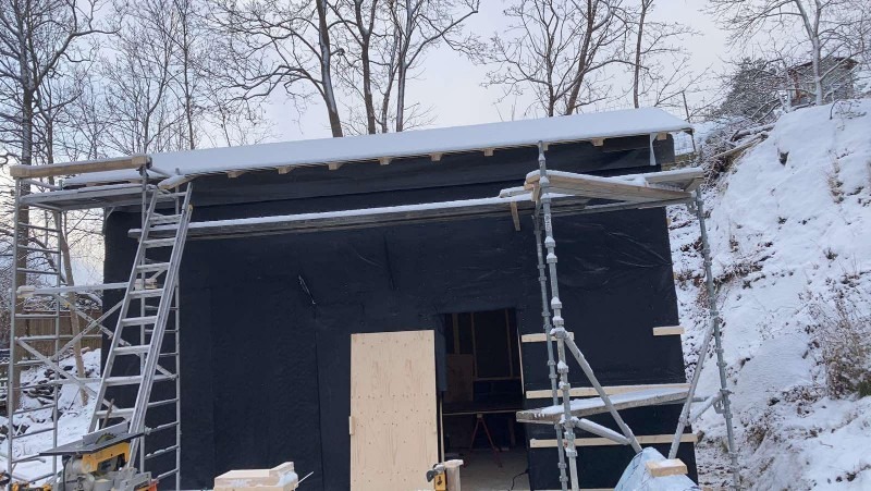 Budynek w trakcie prac elewacyjnych zimą, widoczne rusztowania, czarna membrana, częściowo zamontowana płyta, oraz narzędzia