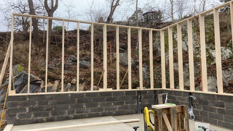 Konstrukcja szkieletowa drewniana na fundamencie z bloczków betonowych, widok na zbocze porośnięte roślinnością.