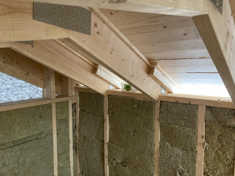 Wnętrze poddasza w trakcie prac: drewniana konstrukcja dachu z metalowymi łącznikami, ściany wypełnione wełną mineralną, widoczne elementy szkieletu drewnianego.