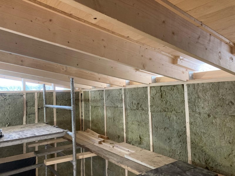 Wnętrze w trakcie prac w Wielkim Klinczu: ściany z izolacją z wełny mineralnej, widoczne drewniane belki stropowe i fragment rusztowania.