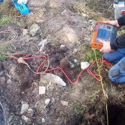 DSWG usługi elektryczne Goleniów - Pomiar rezystancji uziomu w wykopie, z użyciem miernika i sondy, na trawiastym terenie.