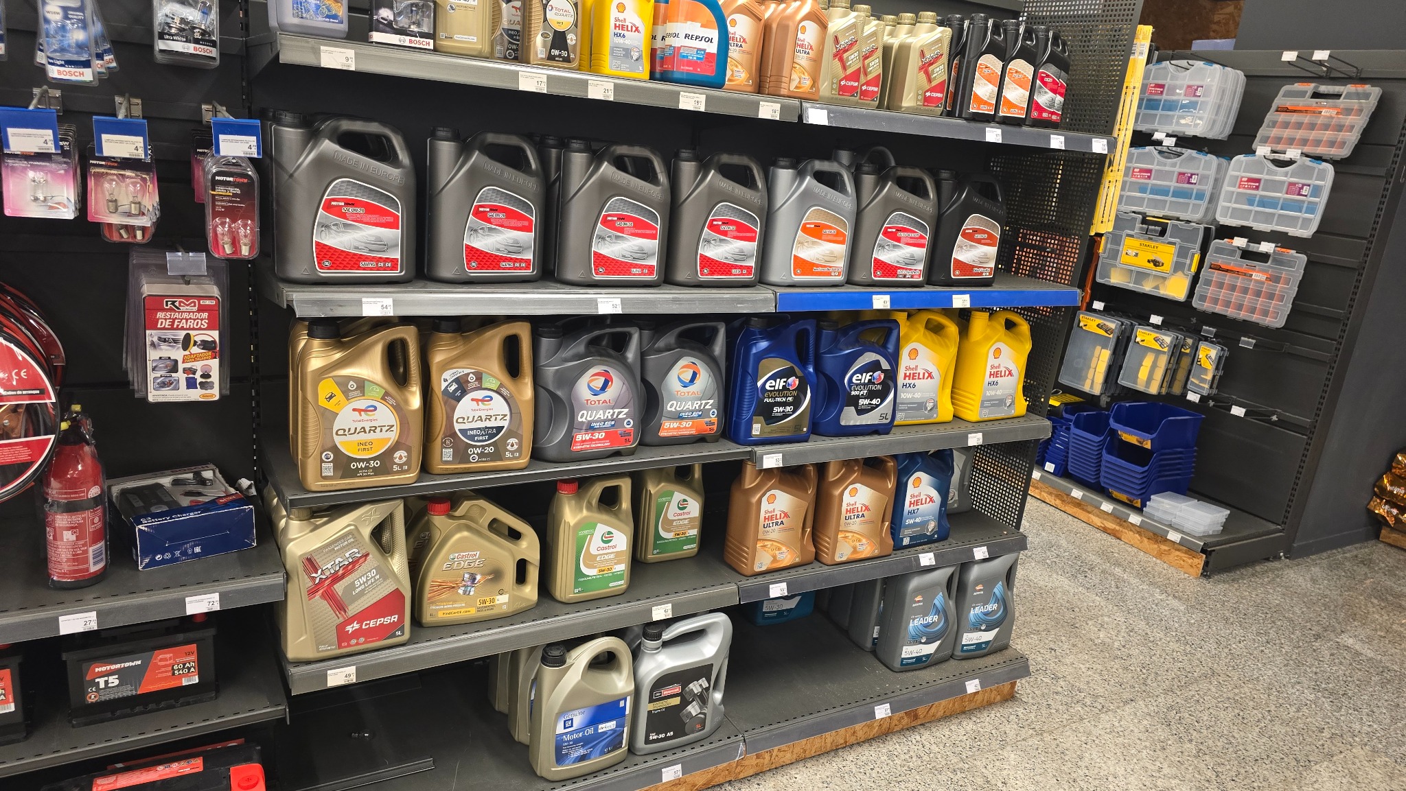 Półki sklepowe z olejami silnikowymi różnych marek i akcesoriami samochodowymi, widok z perspektywy klienta w sklepie motoryzacyjnym.