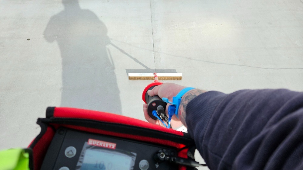 Kontrola szczelności pokrycia dachowego za pomocą szczotki i detektora nieszczelności, widoczny cień osoby obsługującej sprzęt.