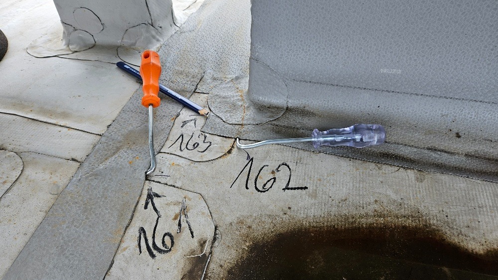 Fragment dachu z papy z odręcznymi numerami, ołówkiem i dwoma różnymi narzędziami z zakrzywionymi końcówkami.