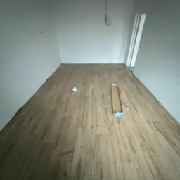 Układanie paneli podłogowych w jasnym pomieszczeniu. Widoczna kartonowa paczka paneli i fragmenty listew. Częściowo ułożona podłoga.