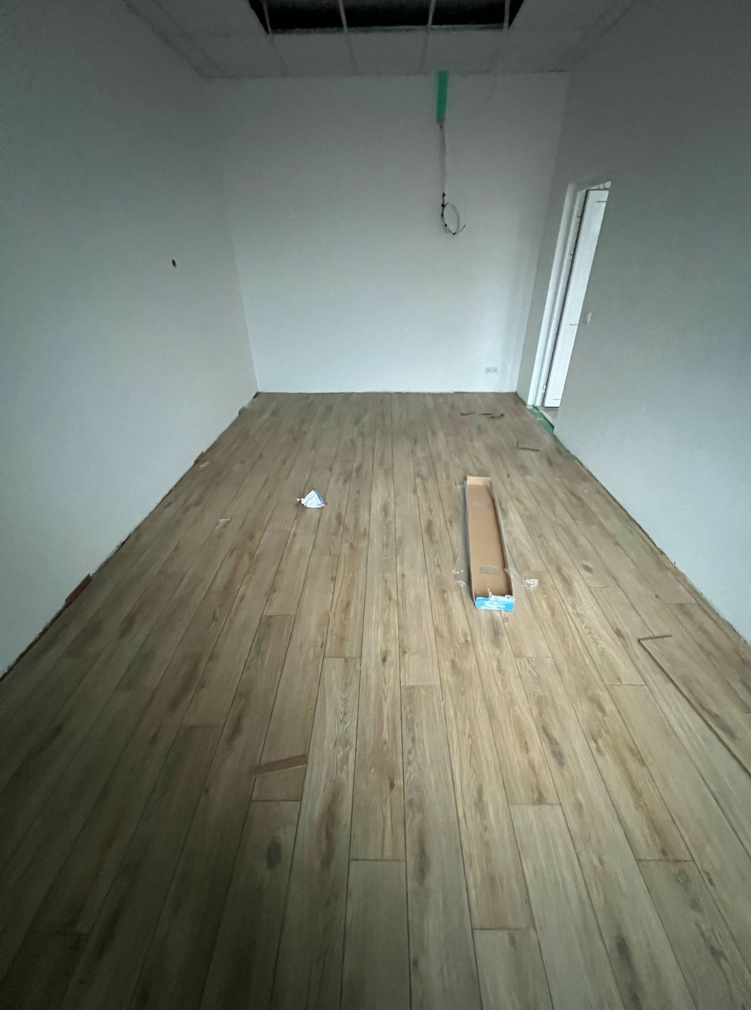 Układanie paneli podłogowych w jasnym pomieszczeniu. Widoczna kartonowa paczka paneli i fragmenty listew. Częściowo ułożona podłoga.